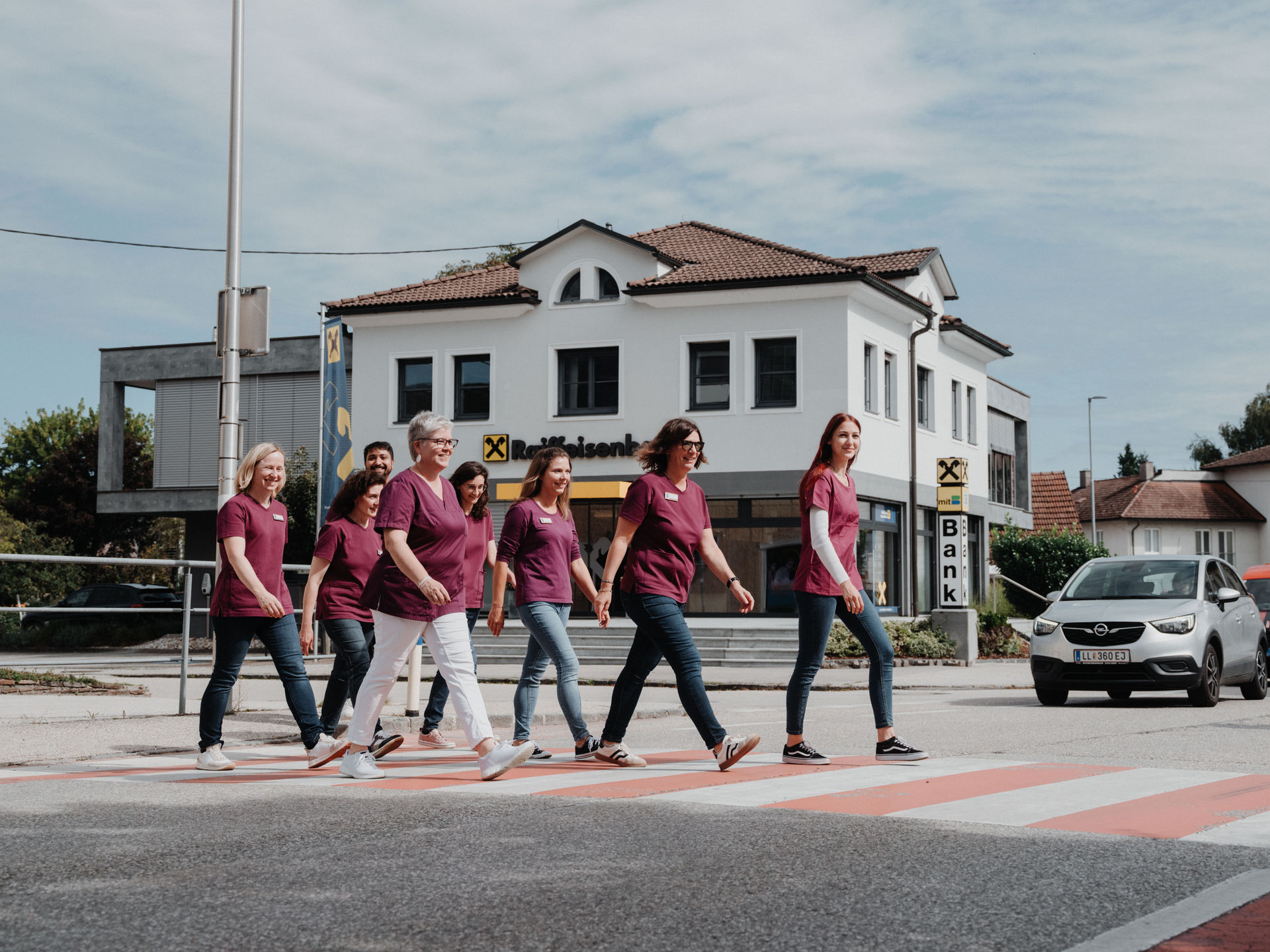 Mehrere Personen in burgunderroten T-Shirts überqueren einen Zebrastreifen vor einem Gebäude mit der Aufschrift 