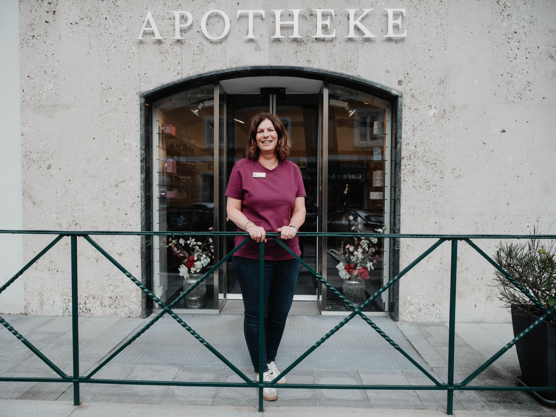 Eine Person in steht an ein Geländer gelehnt vor dem Geschäftslokal der Apotheke